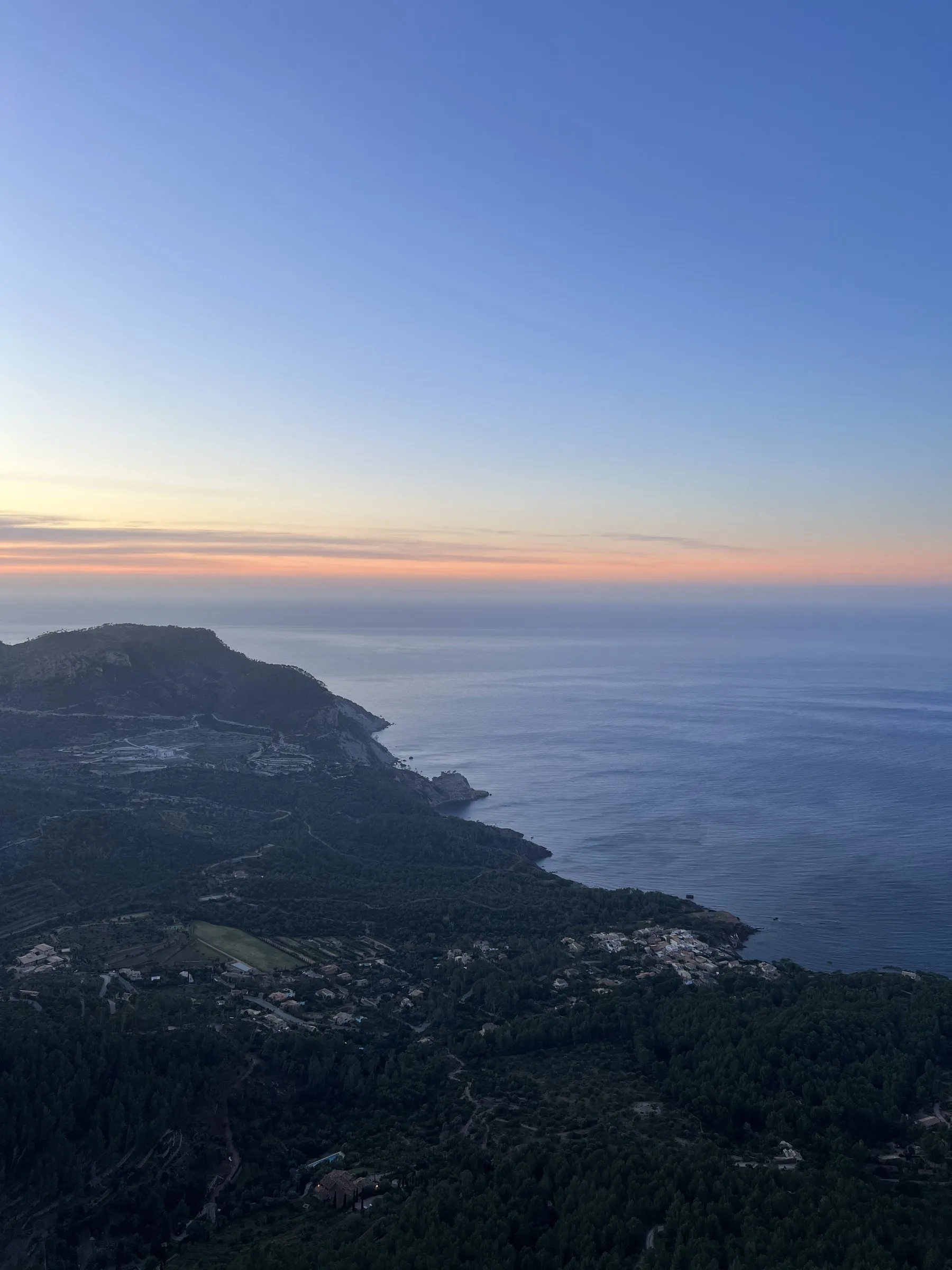 La costa de Banyalbufar al atardecer, con los bancales bajando hacia el mar y un cabo recortado sobre el agua.