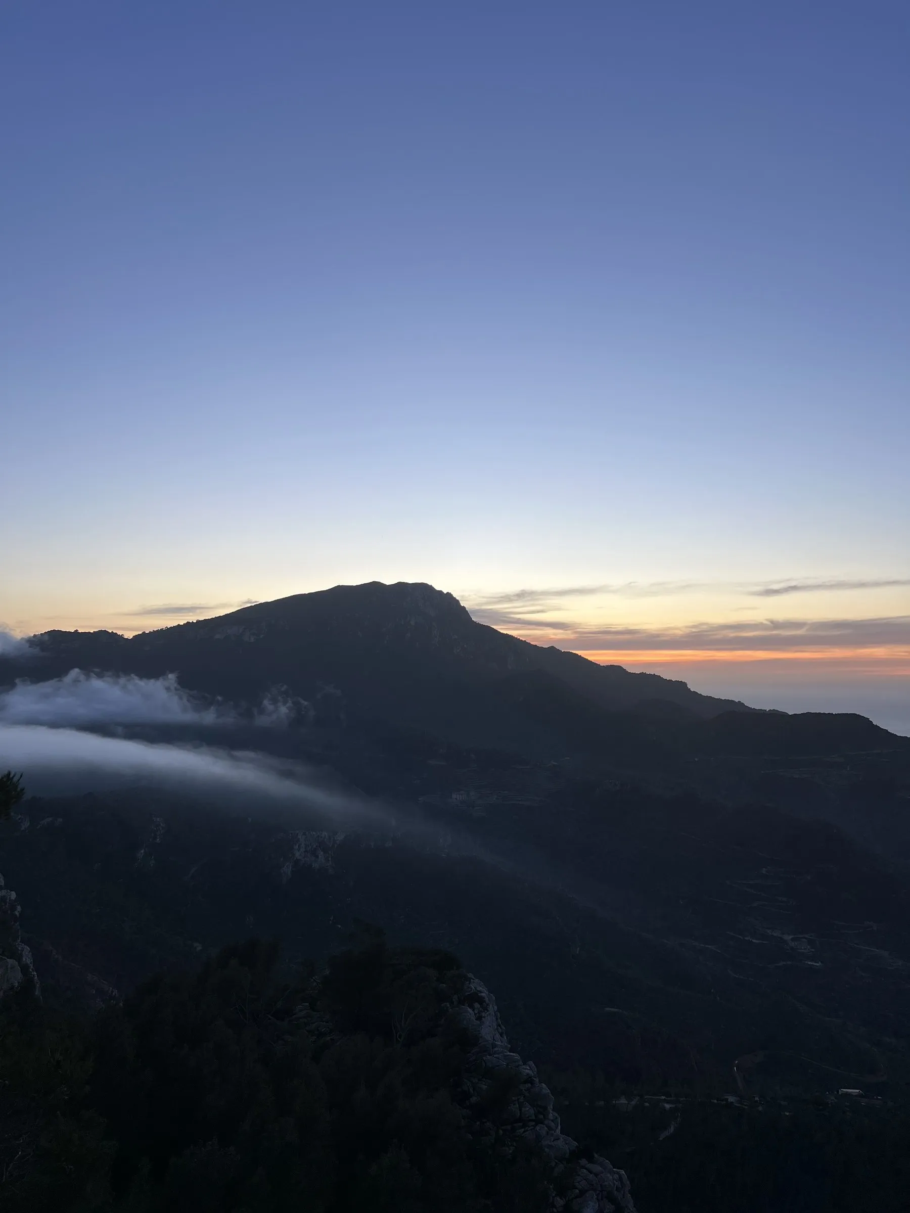 Una lengua de niebla baja deslizándose por la ladera de la montaña sobre Banyalbufar al ponerse el sol.