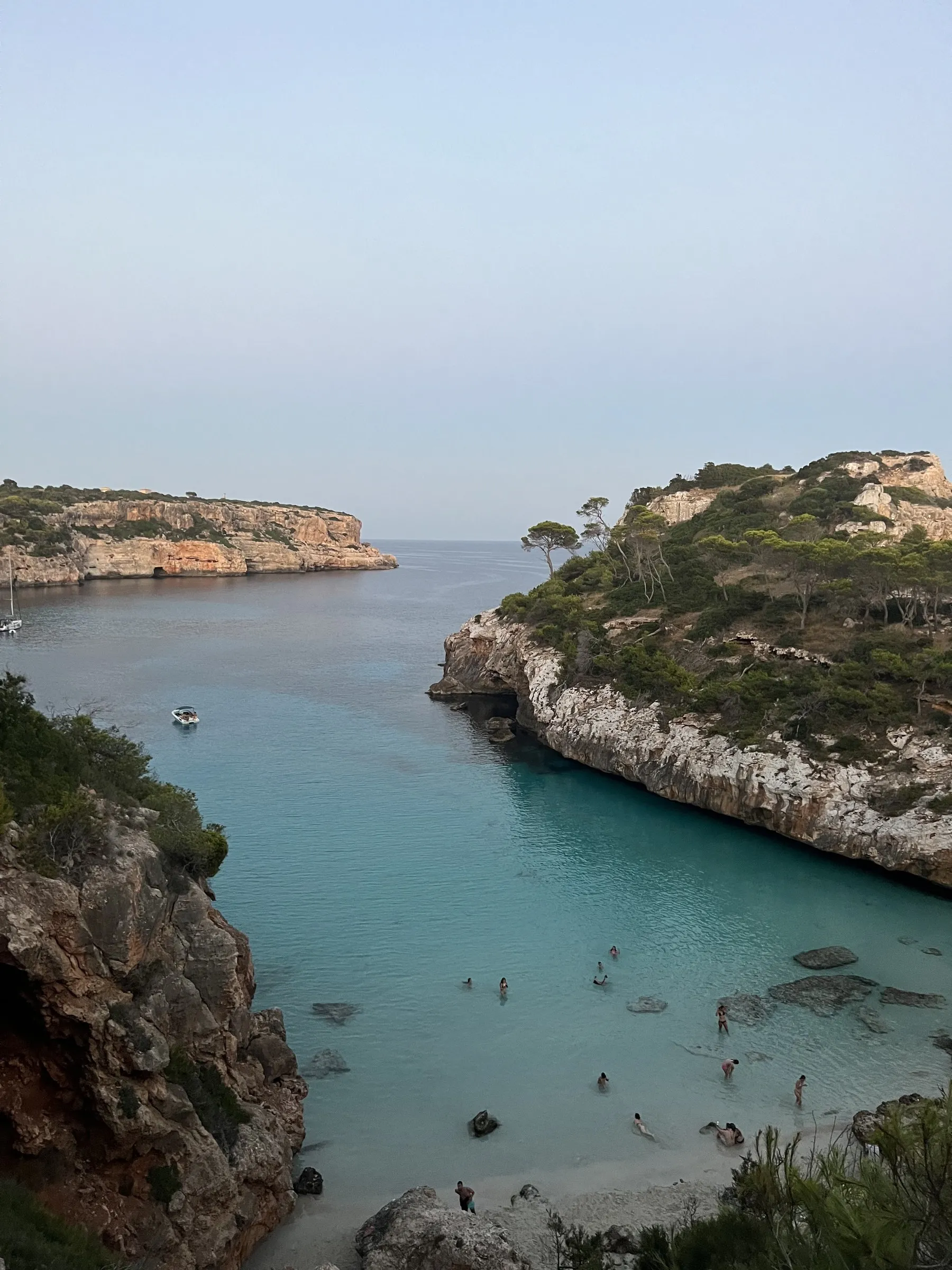 La lengua de arena del Caló des Moro encajada entre acantilados, con bañistas en el agua turquesa y una barca fondeada.