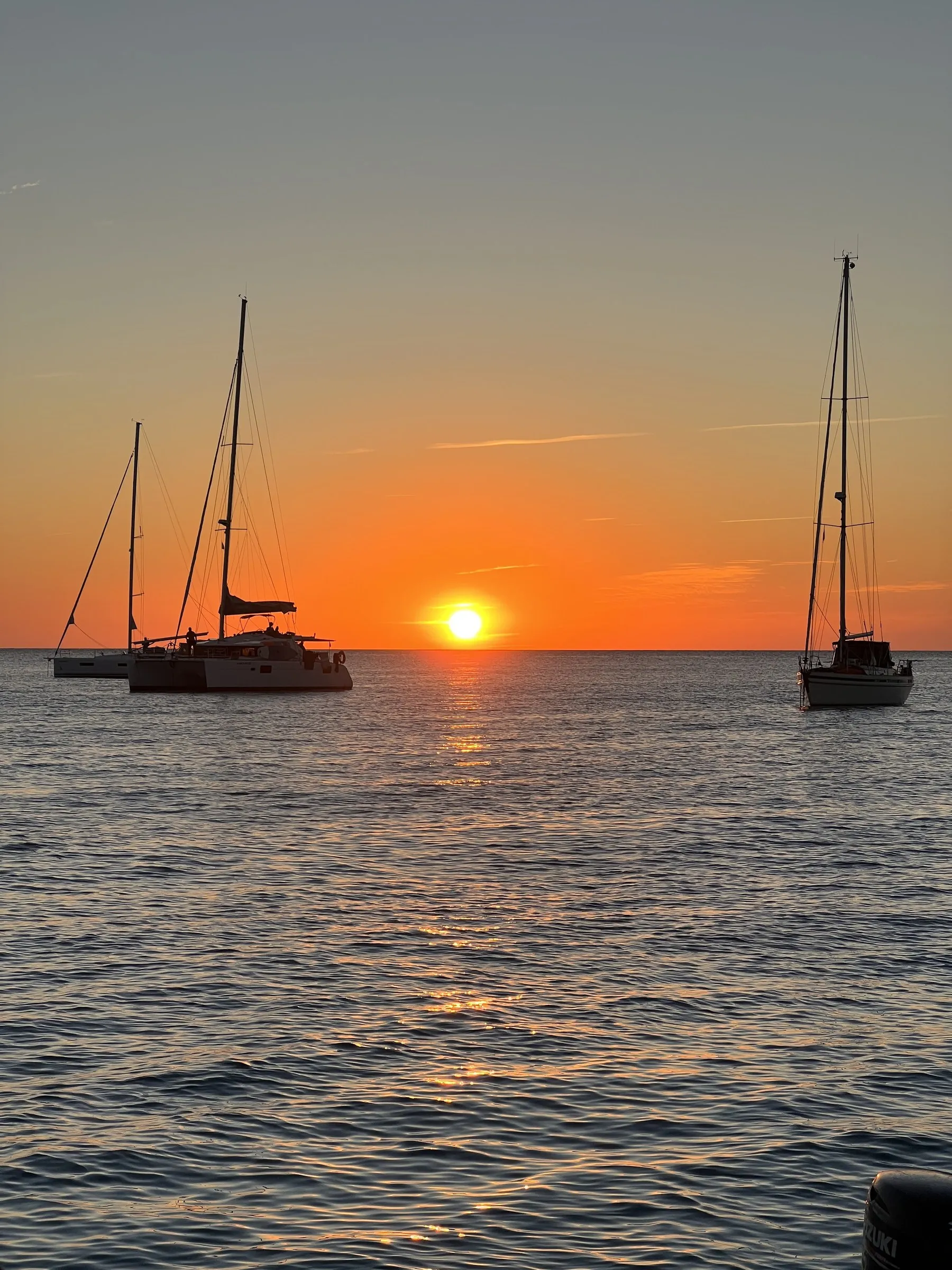Dos veleros fondeados recortados contra el sol poniéndose en el mar frente al Cap de ses Salines.