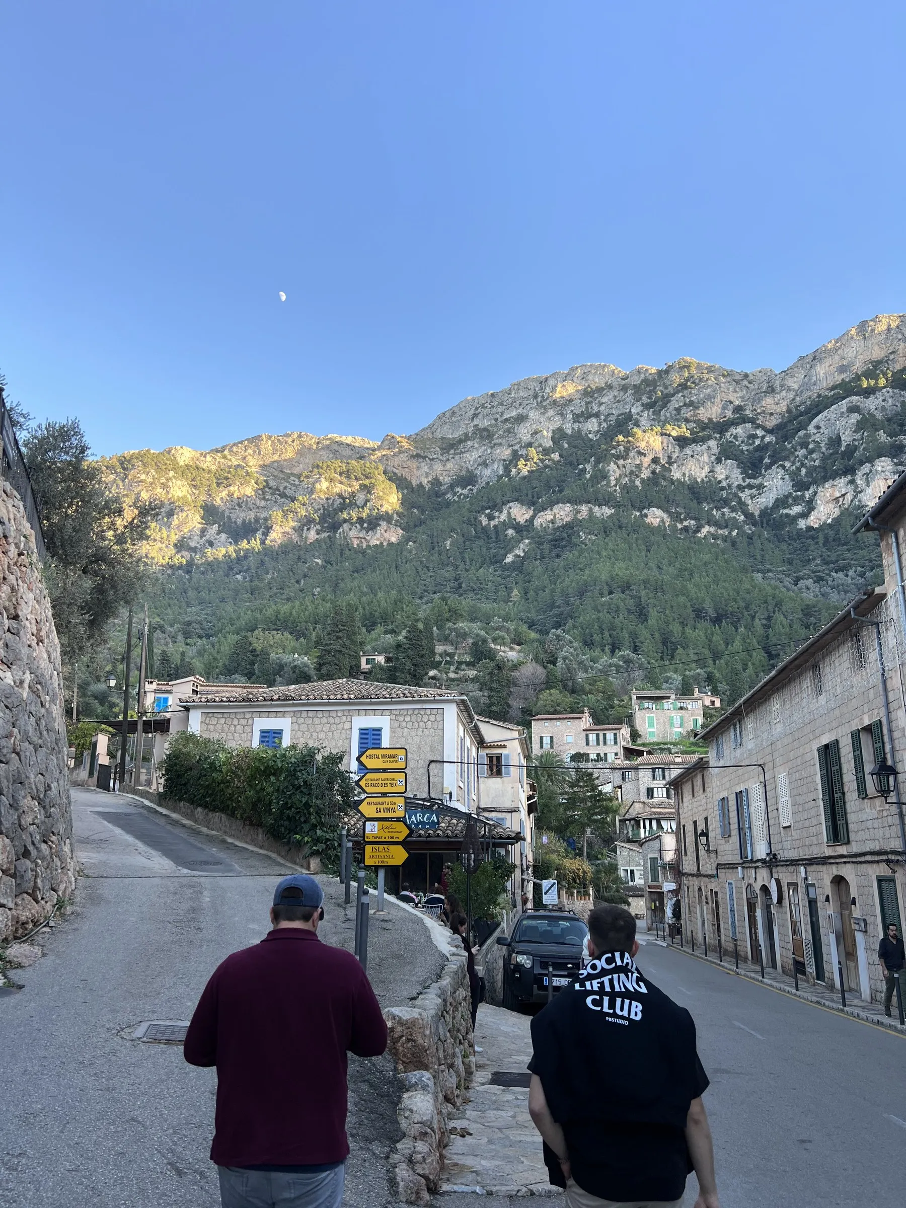 Die Hauptstraße von Deià an einem Winternachmittag, mit Steinhäusern und dem Gebirge im letzten Sonnenlicht.