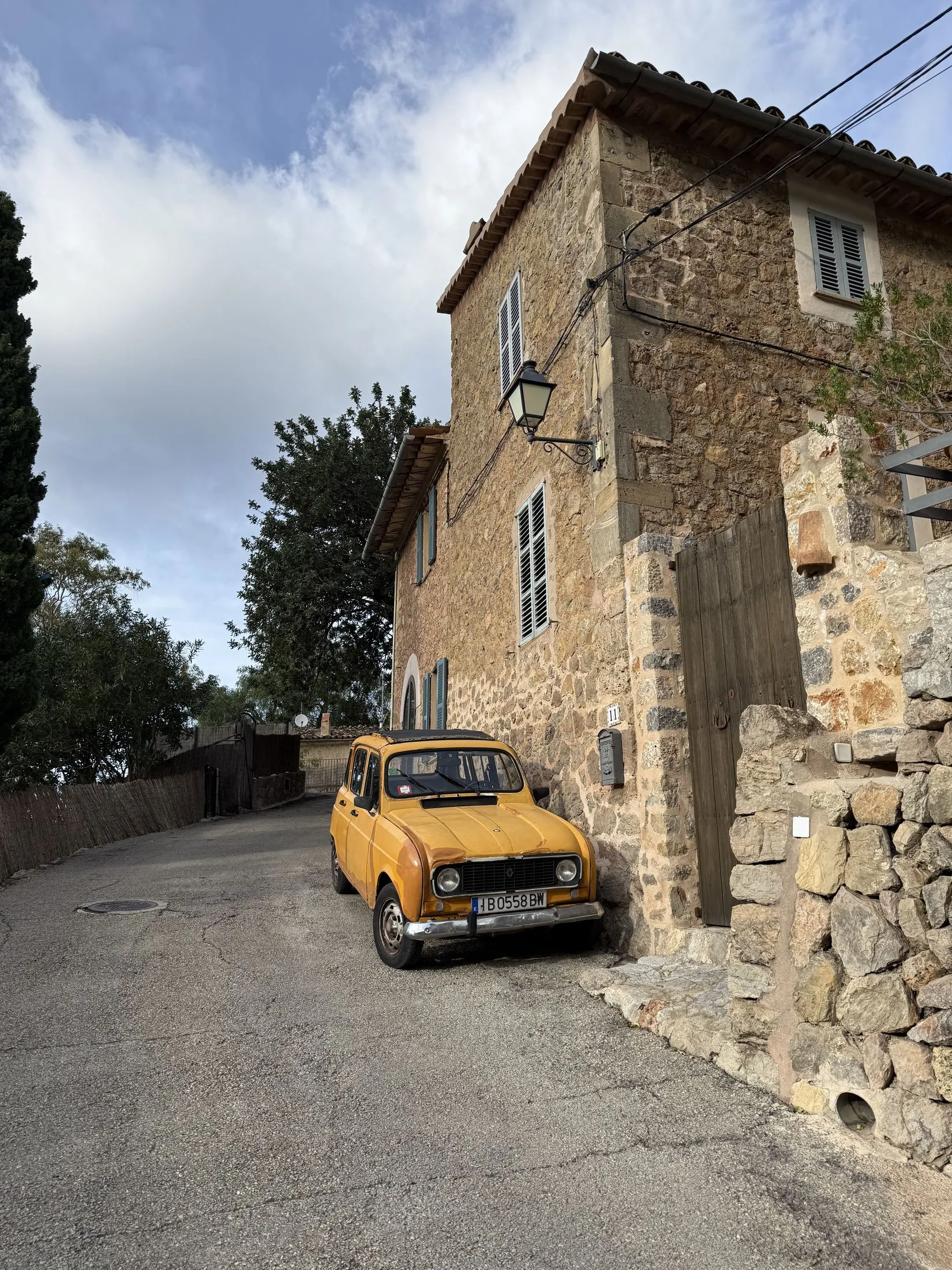 Ein Steinhaus an einer steilen Gasse in Deià, davor ein gelber Oldtimer