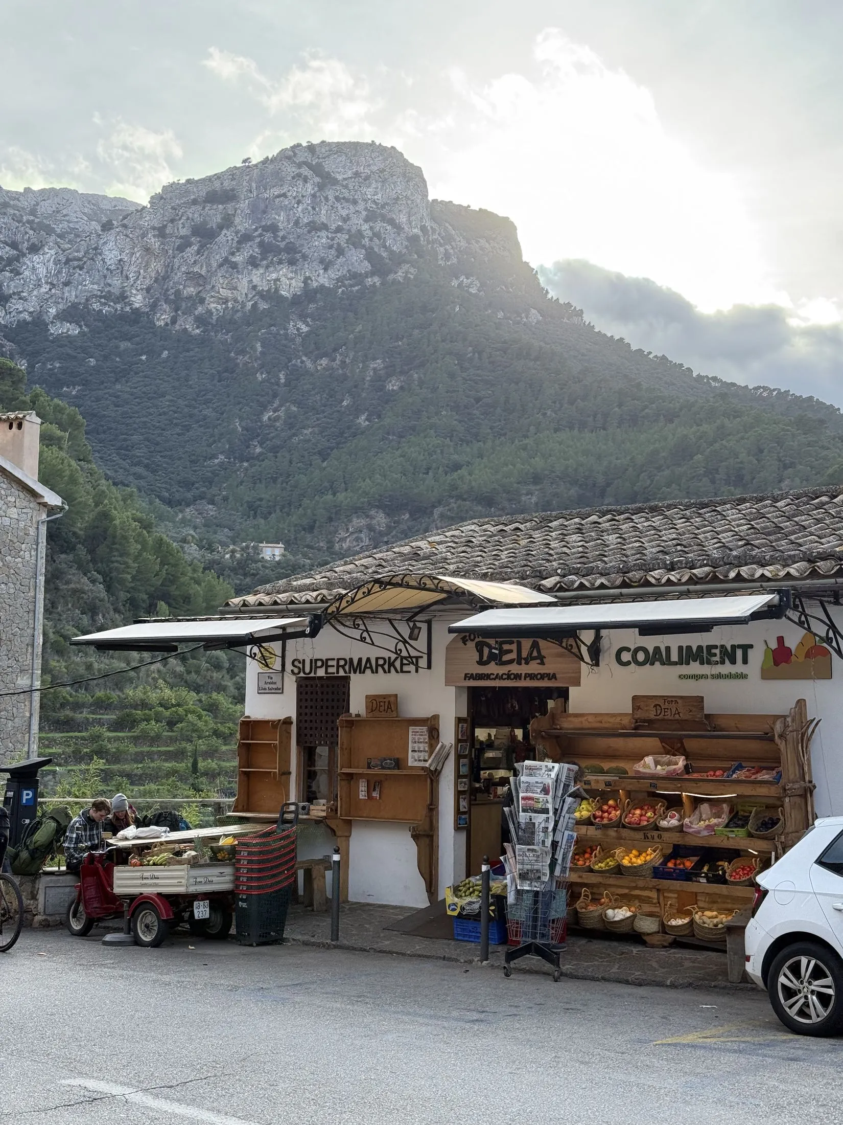 Ein Lebensmittelladen an der Hauptstraße von Deià, dahinter erhebt sich der Bergstock des Teix direkt über dem Dorf.