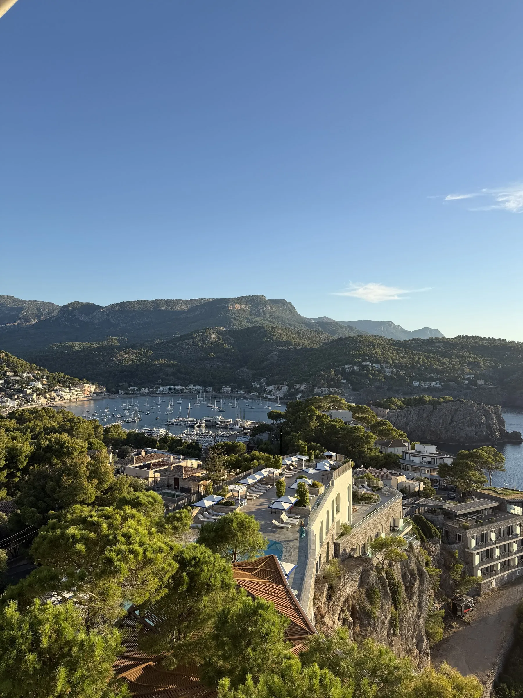 La terraza escalonada del hotel sobre el acantilado y, al fondo, el puerto de Sóller con la sierra de Tramuntana