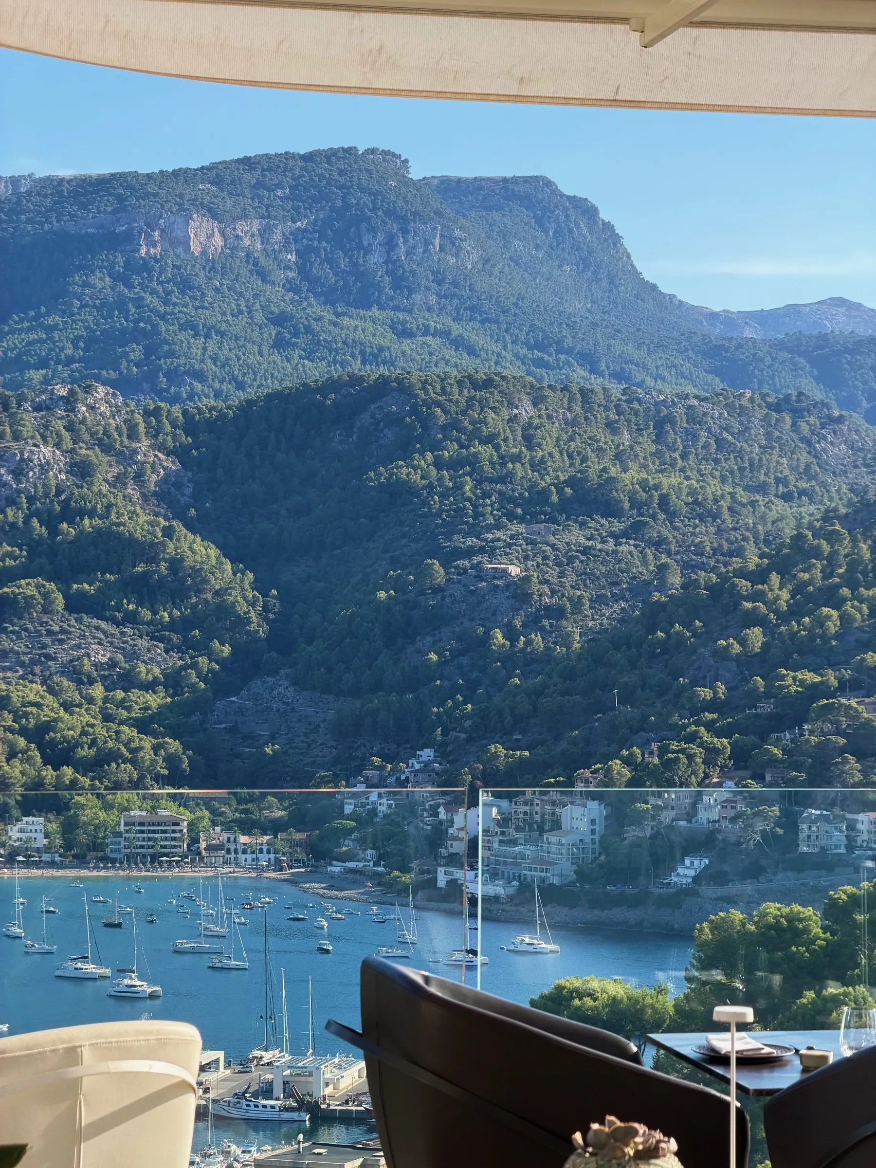 La bahía de Port de Sóller llena de veleros fondeados, vista desde la terraza bajo el toldo