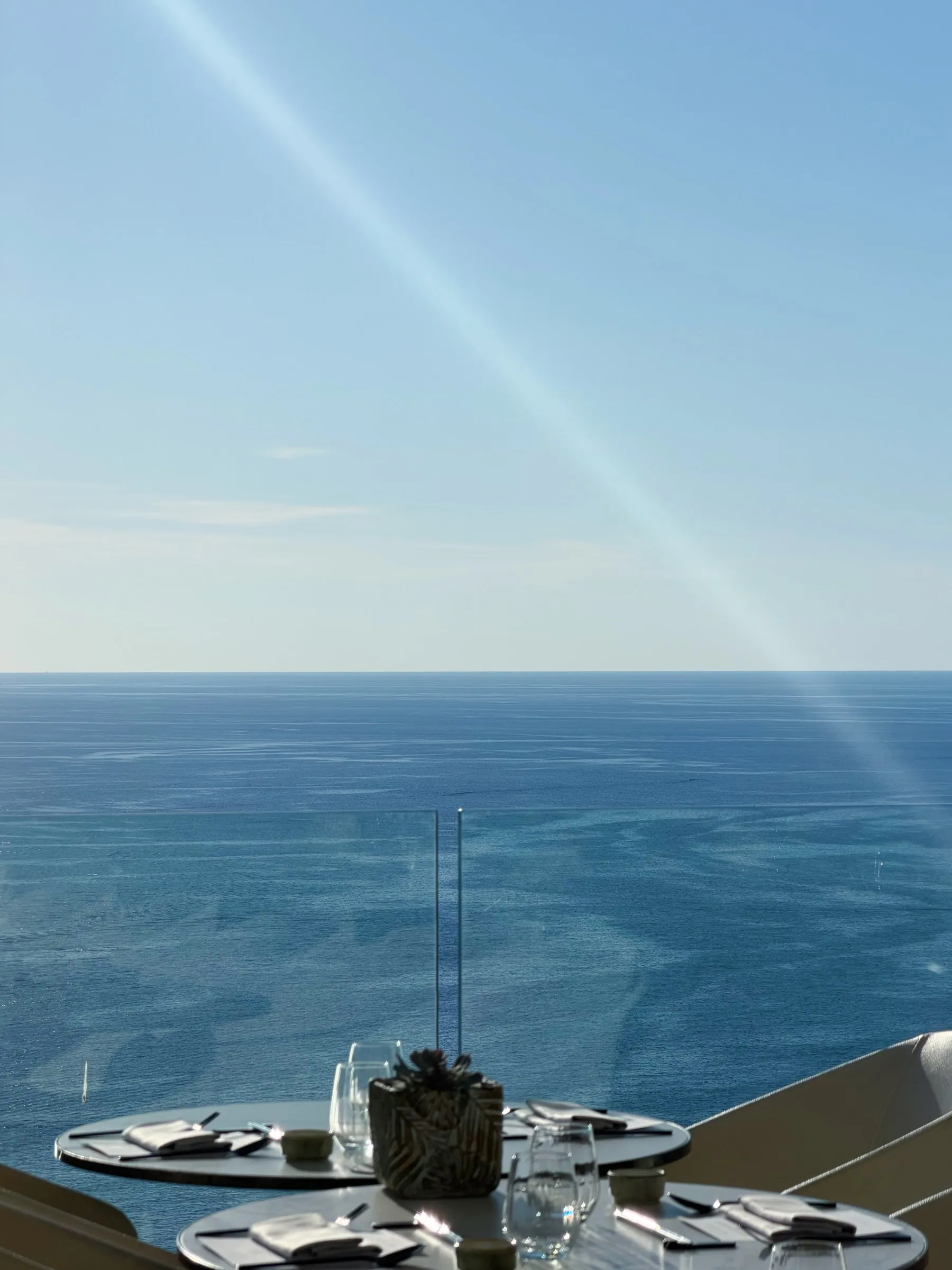 Dos mesas redondas preparadas al borde de la terraza, con el mar abierto ocupando todo el fondo